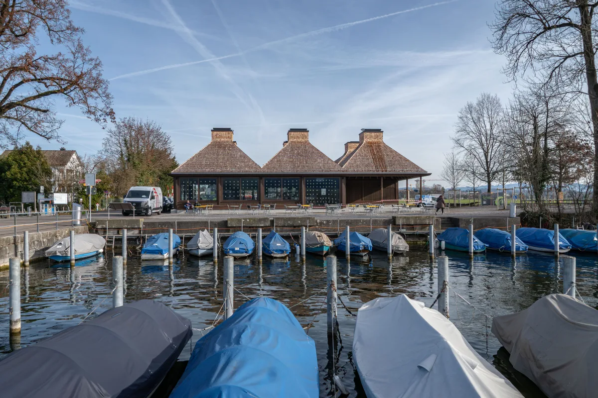 «Das ist keine architektonische Dutzendware», sagt Stadtrat Cla Famos über den Bau des Architekturbüros Fiechter & Salzmann. Das Seerestaurant «im Schilf» in Uster von aussen: Man sieht das Gebäude mit dem charakteristischen sechsteiligen Dach und davor Boote, die mit blauen Blachen abgedeckt sind.